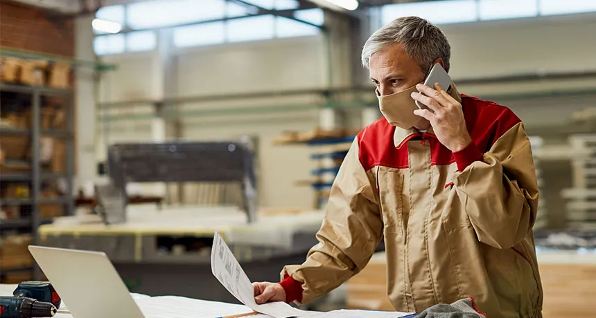 ESG und ISO Branchenlösung Bauwirtschaft, Mehrwert durchgängige Lieferkettentransparenz, Mann in Holz-Lagerhalle in Arbeitskleidung telefoniert und schaut auf Laptop