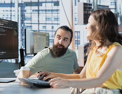 ESG Management Reporting Schnittstellen, Frau und Mann mit Bart schauen auf zwei Computerbildschirme mit Daten