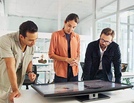 EUDR Compliance Software, Frau und zwei Männer stehen vor liegendem Bildschirm mit Geo- und Lieferketten Daten