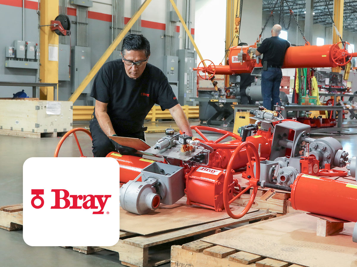 Interview Bray International Titelbild, Bray Logo, Maschinenbauhalle, Mitarbeiter arbeitet an roten Maschinenteilen auf Holzpaletten