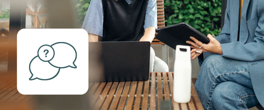 Zwei Personen an einem Tisch, die auf einen Laptop schauen mit Icon mit Gesprächsblasen