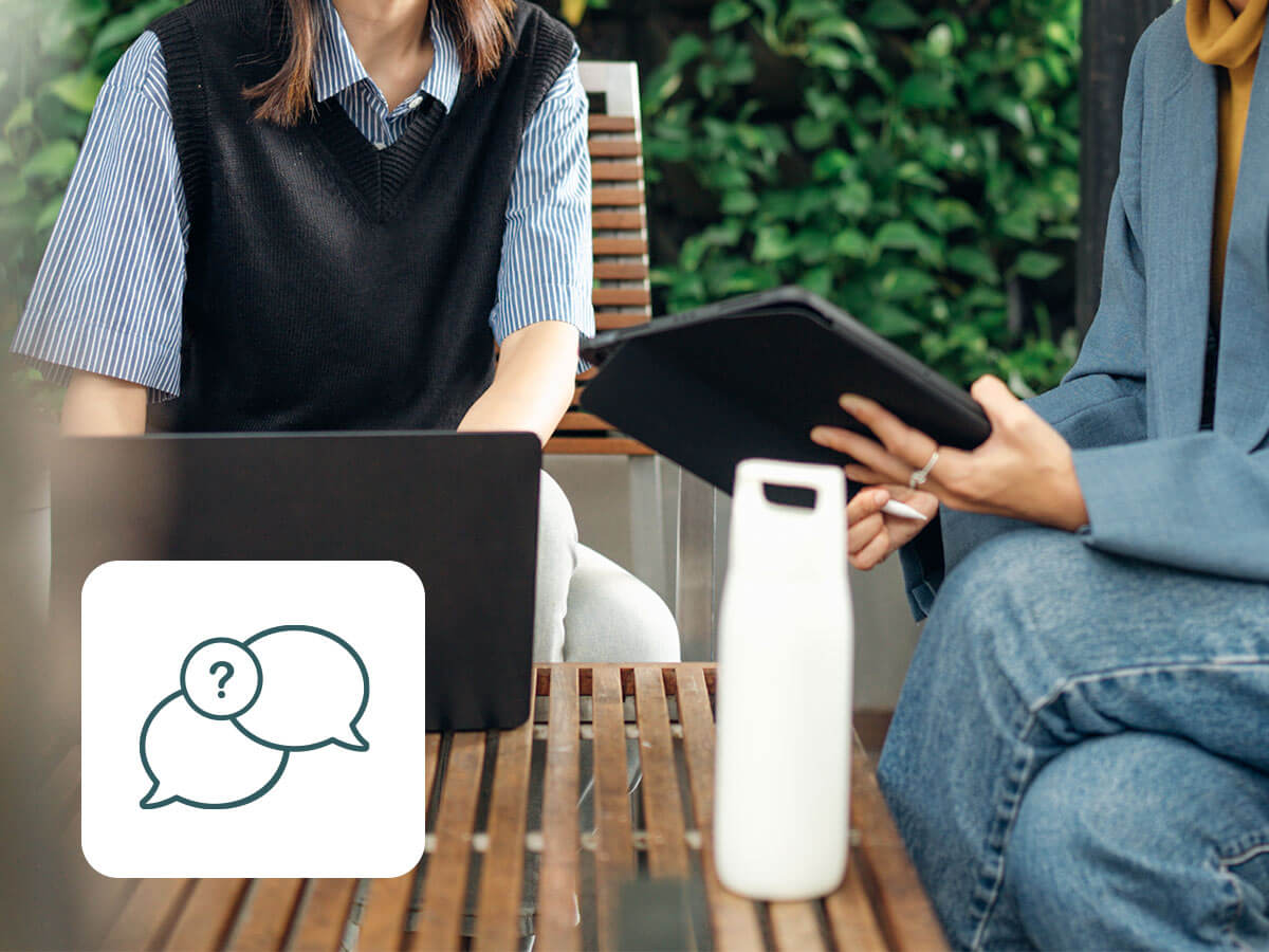 Zwei Personen an einem Tisch, die auf einen Laptop schauen mit Icon mit Gesprächsblasen