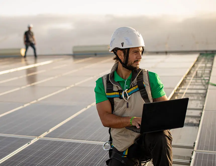 Mitarbeiter mit Laptop und Schutzhelm prüft eine Solaranlage als Teil des betrieblichen Energiemanagements.