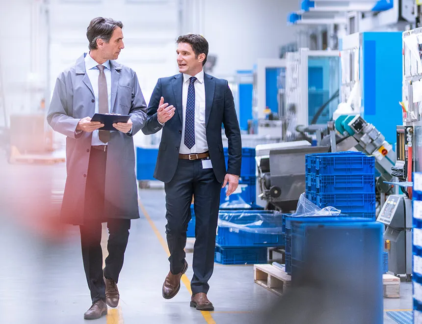 Two employees reviewing processes together in a production hall using a tablet – symbolic image for ISO 9001 quality management.