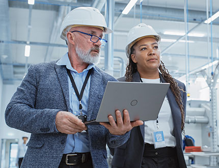 ISO trifft ESG, Contentpiece Checkliste, Mann und Frau mit Laptop in Fabrikhalle