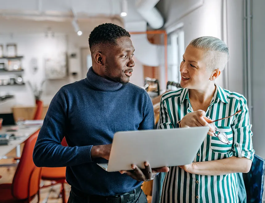 Man and Woman, standing in a modern office, looking at the esg solution EcoVadis on their laptop