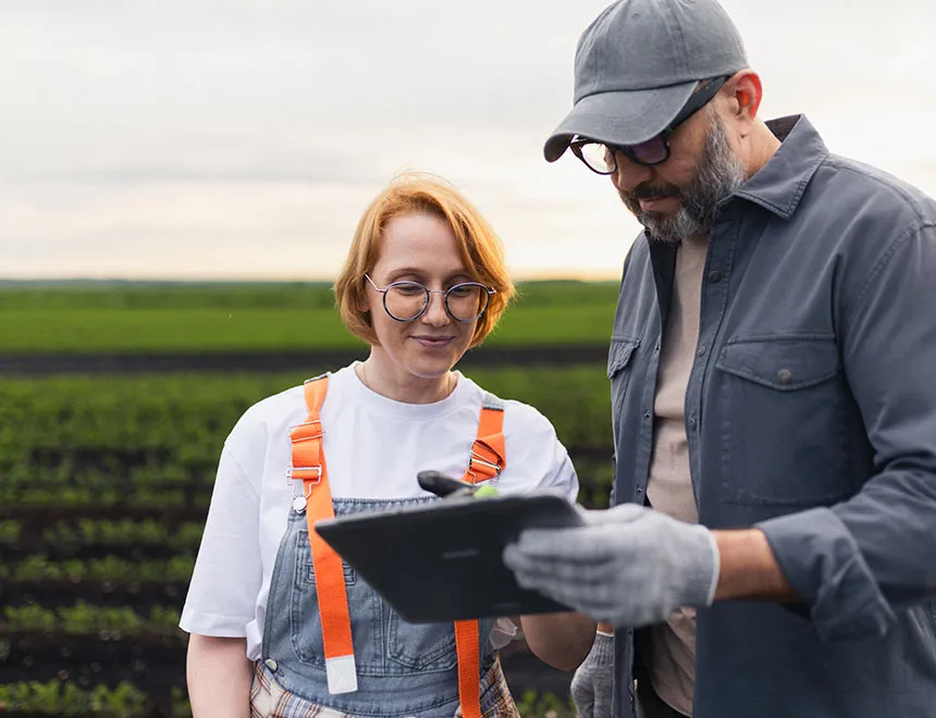 Man and woman in work clothing reviewing data from their esg software on a tablet in an open green field