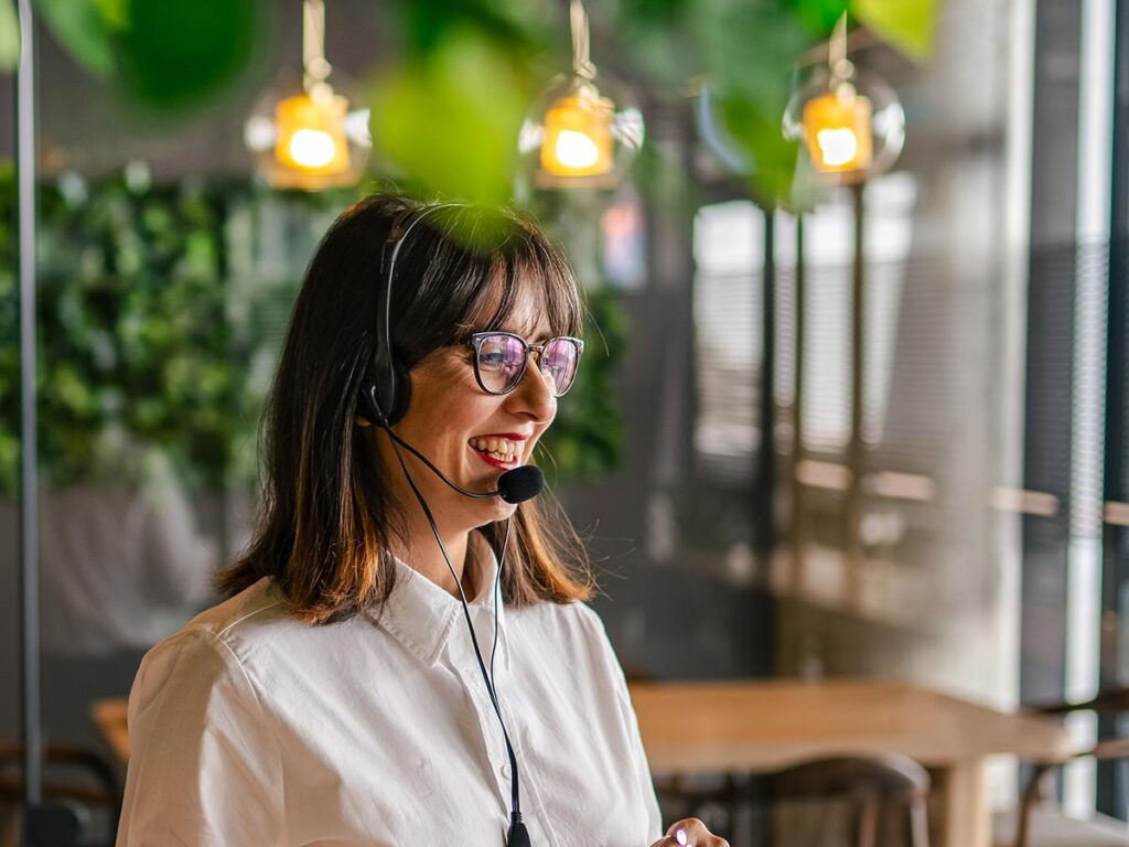 leadity Account Management, freundliche Frau mit Brille und Headset, telefoniert in Büro mit vielen Pflanzen
